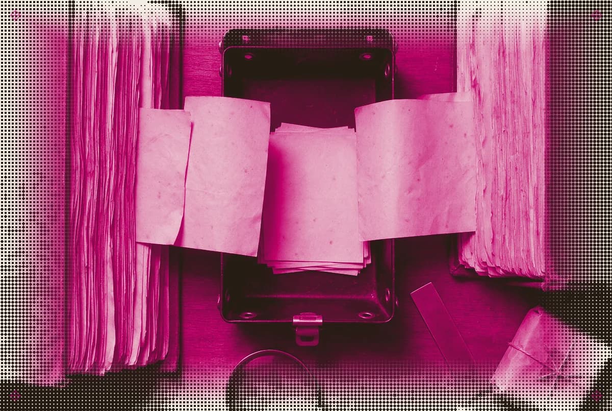 Two worn operating ledgers feeding blank manifests into a shared tray on a 1960s systems desk