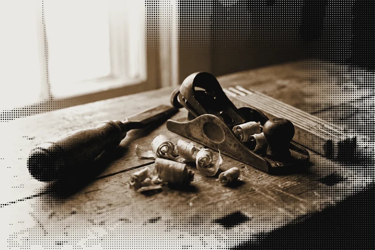 A wooden-handled chisel, a small hand plane and a folding rule on a workbench, pressed in bronze