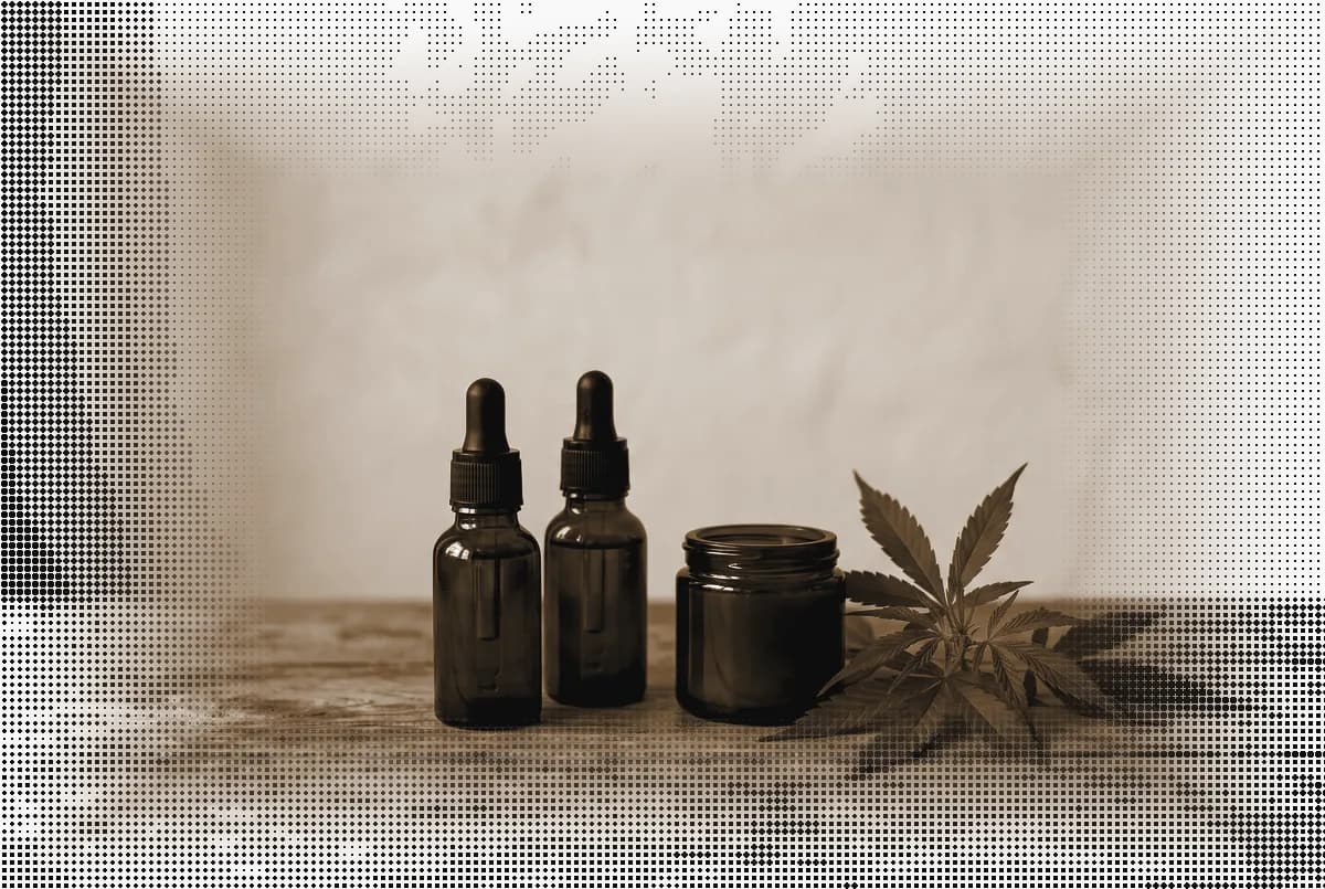 Unlabeled amber dropper bottles and a jar beside a hemp sprig on a shop counter, pressed in bronze