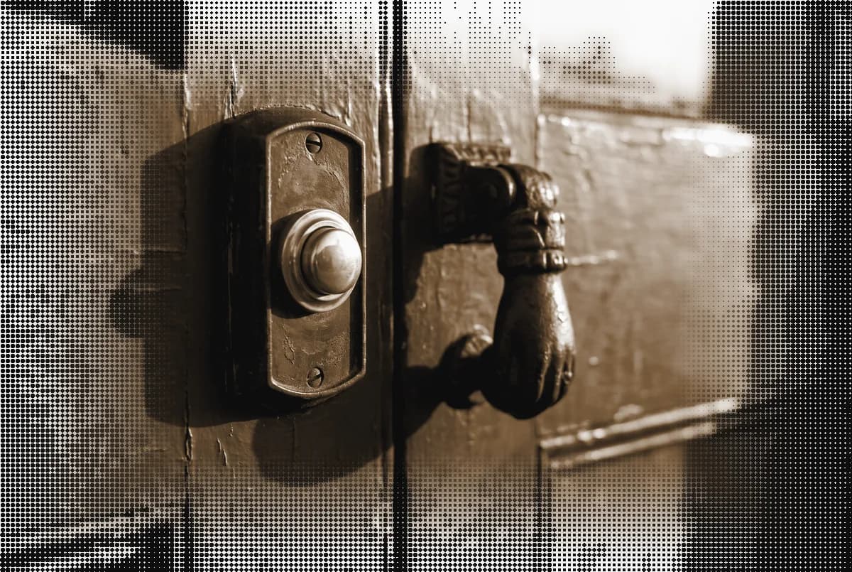 A brass doorbell and a cast-iron knocker on a painted shop door, pressed in bronze