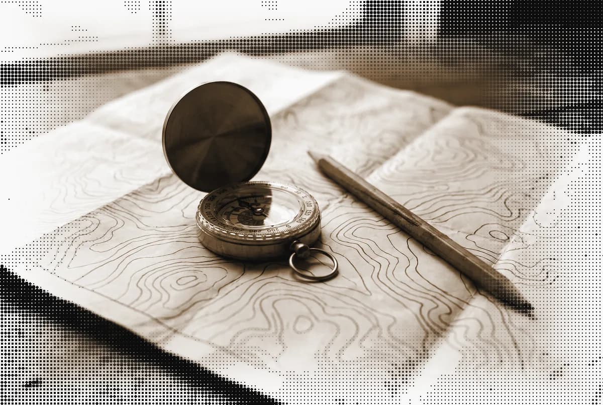 A brass compass open on a contour map with a pencil beside it, pressed in bronze