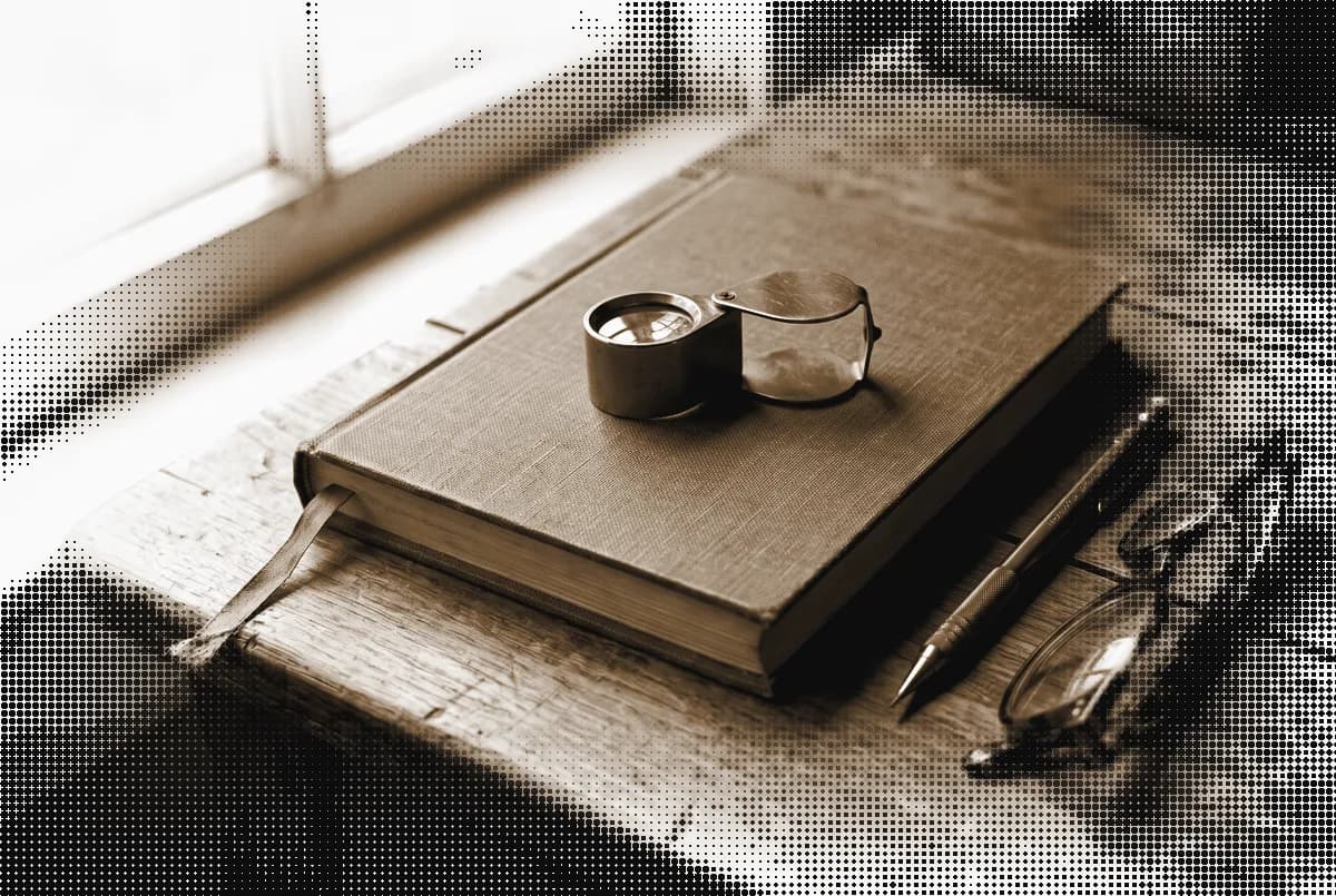 A closed notebook with a brass loupe resting on it, a pencil and a pair of reading glasses on a desk, pressed in bronze